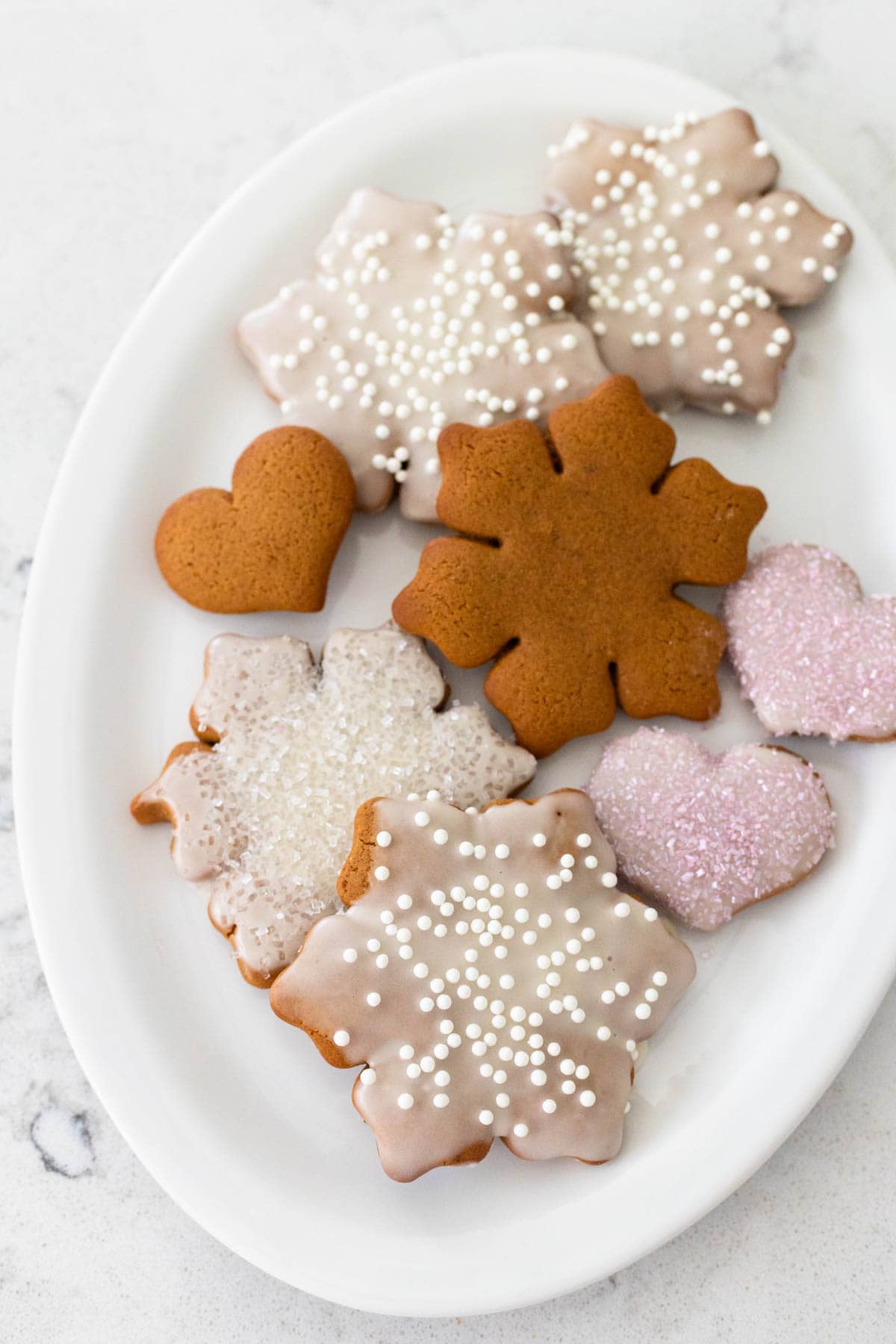 The white oval platter has a selection of iced gingerbread cookies in snowflake and mini heart shapes.