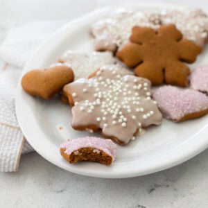 A white platter is filled with frosted gingerbread cookies cut into snowflake and heart shapes.