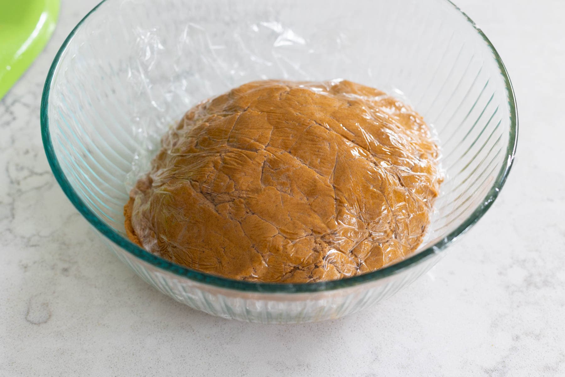 The prepared gingerbread cookie dough is in a large mixing bowl covered in plastic wrap.