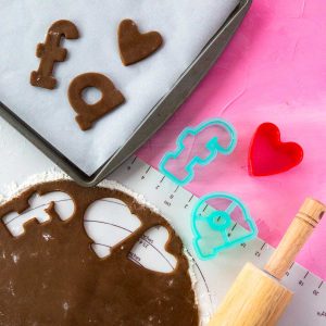 Gingerbread cookie dough is rolled out and has a few letter shapes cut out and put on a baking pan.