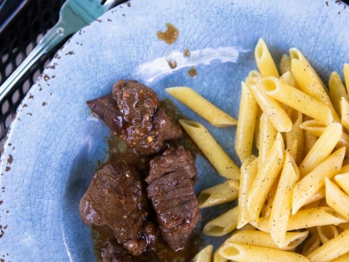 Marinated steak on a plate next to buttered noodles.