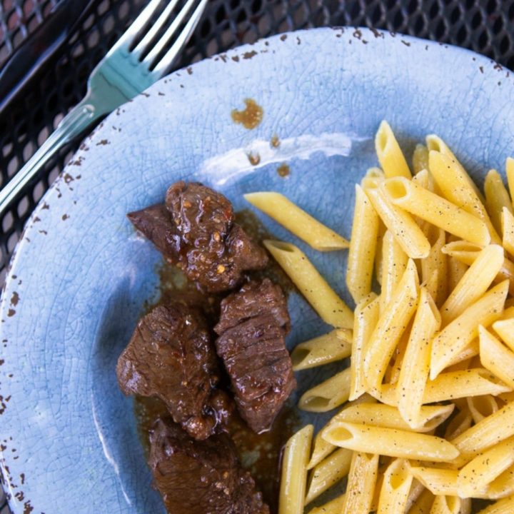 Marinated steak on a plate next to buttered noodles.