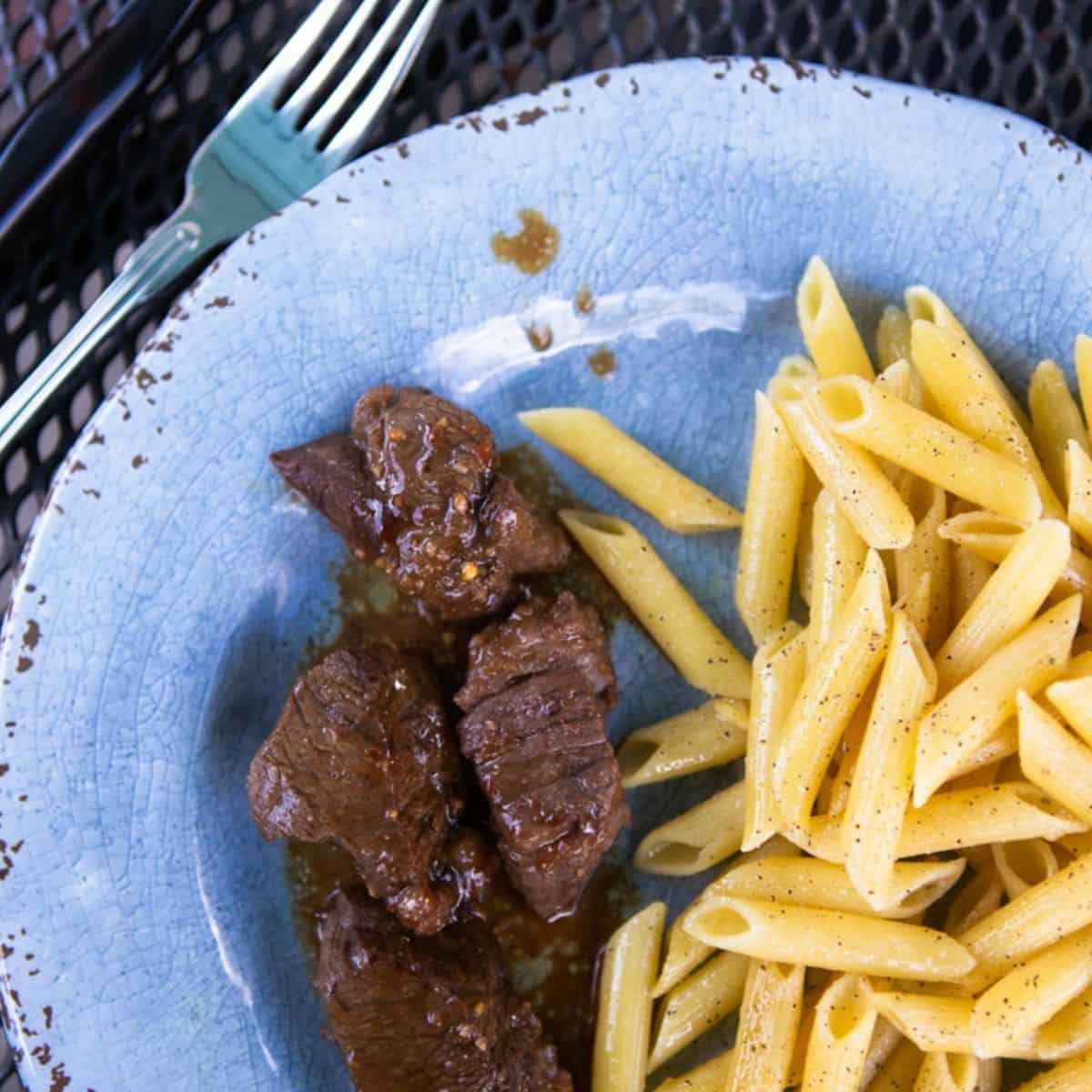 Marinated steak on a plate next to buttered noodles.