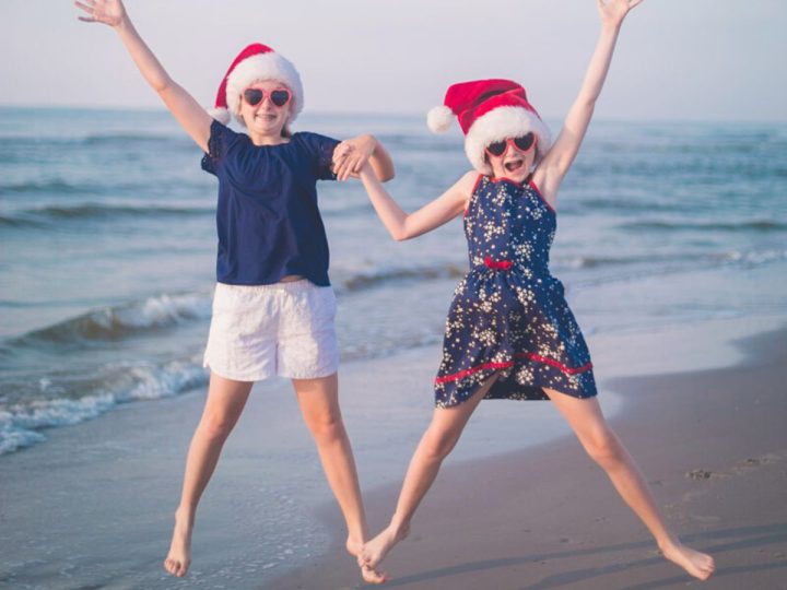 Two young girls wearing Santa hats jumping on a beach