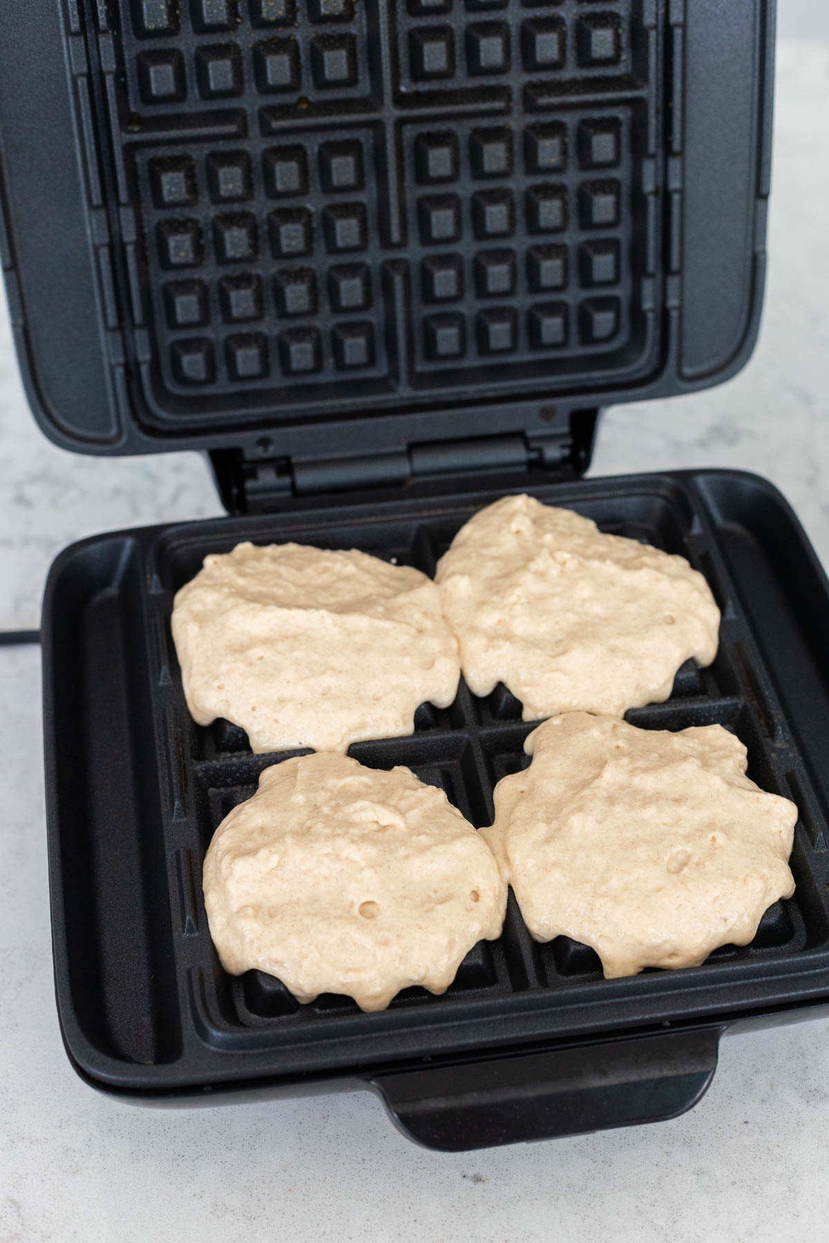 The waffle iron has been filled with 4 scoops of waffle batter.