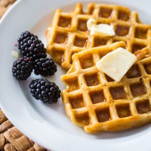 A plate with two waffles topped with butter and a side of blackberries.