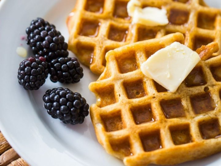 A plate with two waffles topped with butter and a side of blackberries.