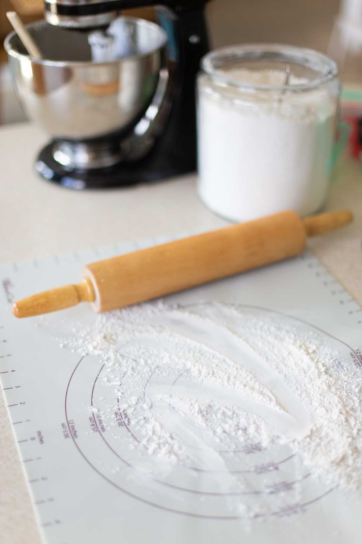 A baking mat sprinkled with flour has a rolling pin and stand mixer in the background.