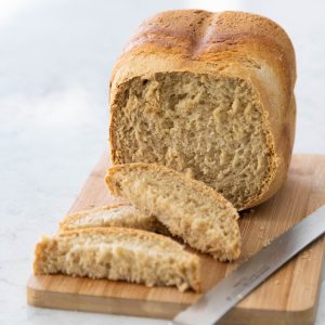 A loaf of apple bread sits on a cutting board by a bread knife.