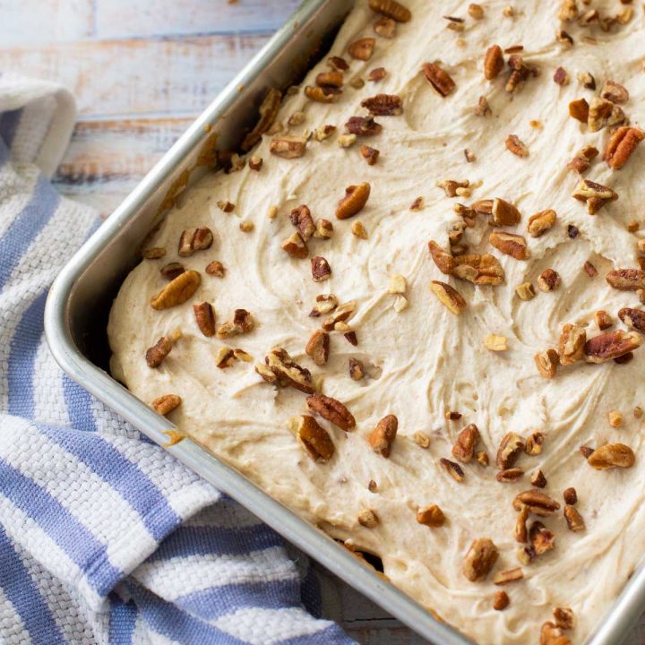 A metal baking pan filled with a sheet cake topped with browned butter frosting and chopped pecans.