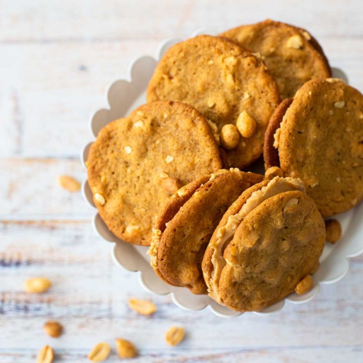 A platter of crunchy peanut butter sandwich cookies next to a scattering of peanuts.