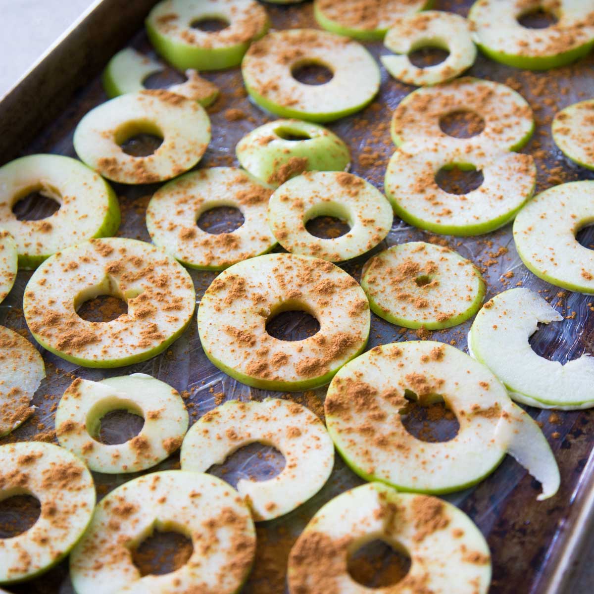 A baking pan has thinly sliced apple circles sprinkled with cinnamon ready for baking.