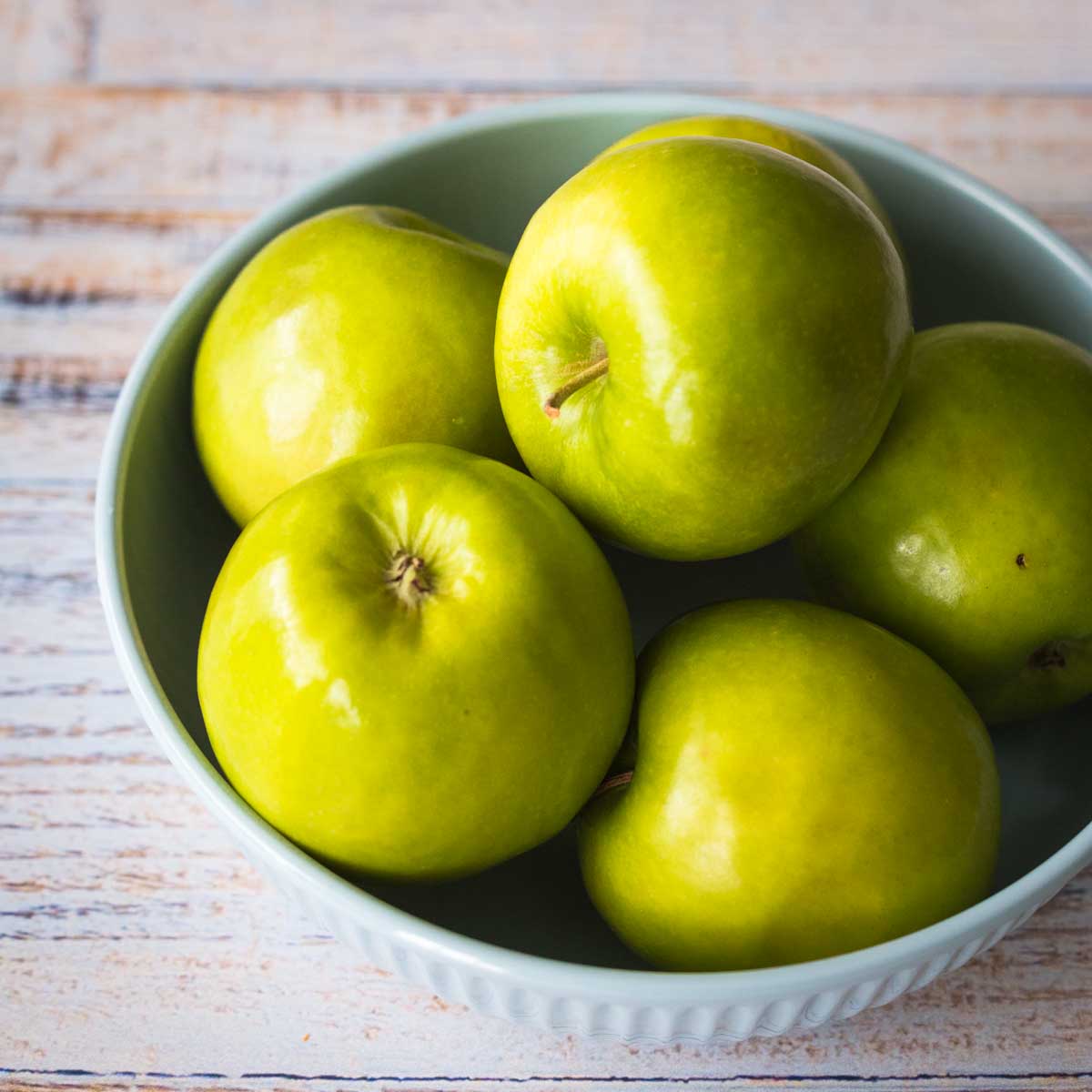 A bowl full of Granny Smith apples sits on a table.