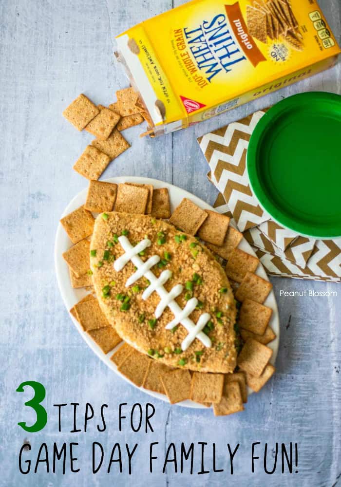 A football shaped cheeseball on the table with napkins, plates, and crackers.