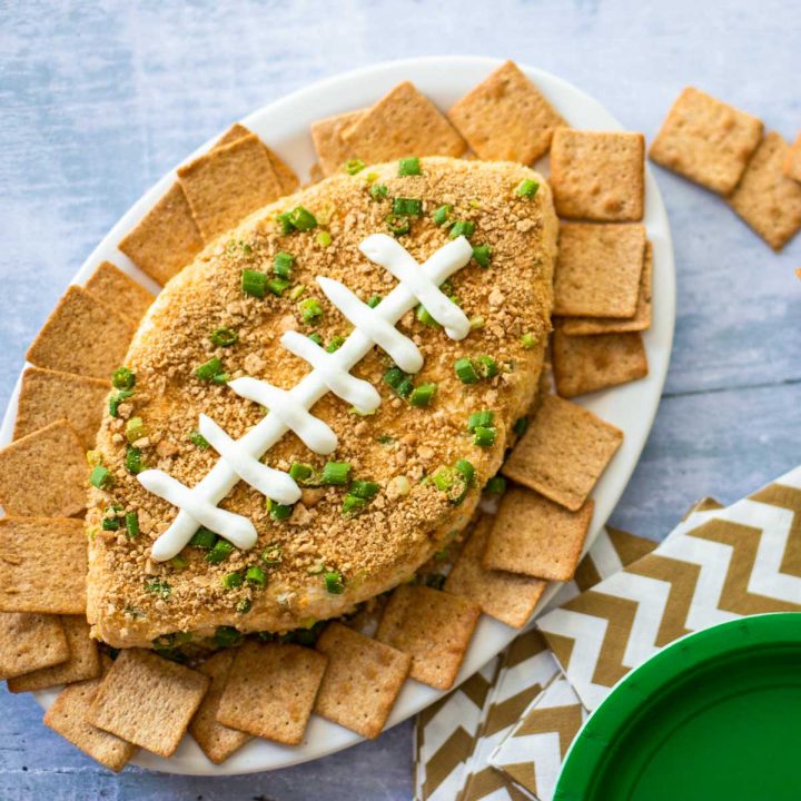 A football-shaped jalepeno popper cheeseball has a sour cream decoration for the laces and is surrounded by Wheat Thin creackers.