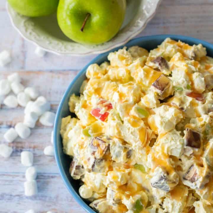 A bowl of creamy Snicker salad has apples, marshmallows, Snickers tossed together.