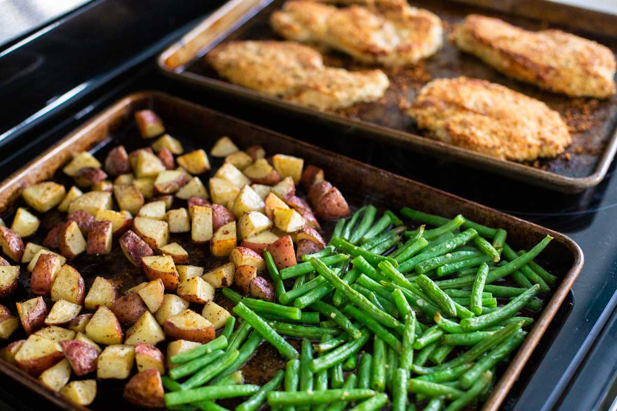 The baking sheet has green beans, chopped potatoes, and chicken.