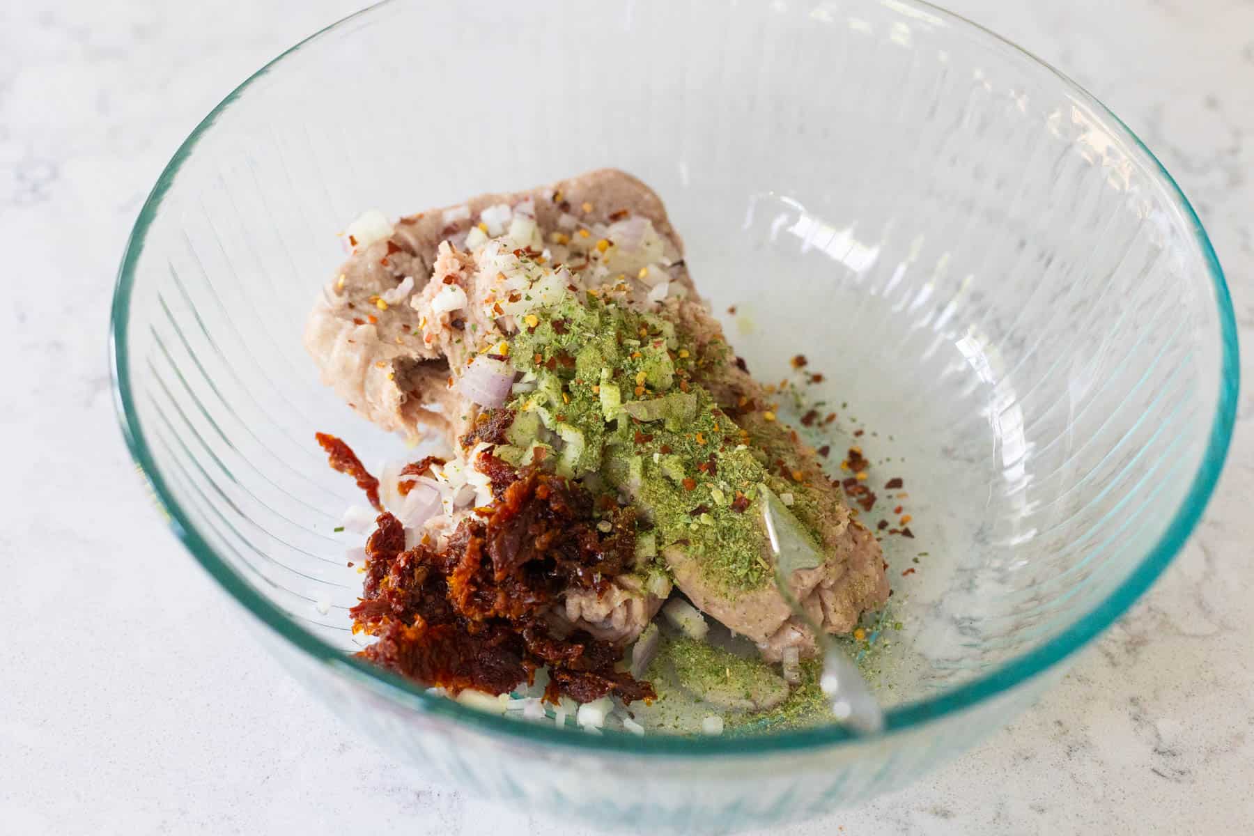 The ground turkey meat is in a large mixing bowl. The chopped tomatoes and seasonings are sprinkled over the top.