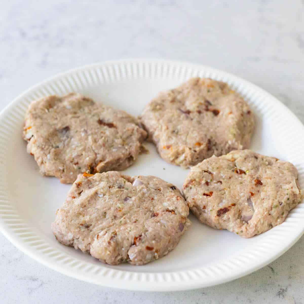 There are four burger patties on a plate.