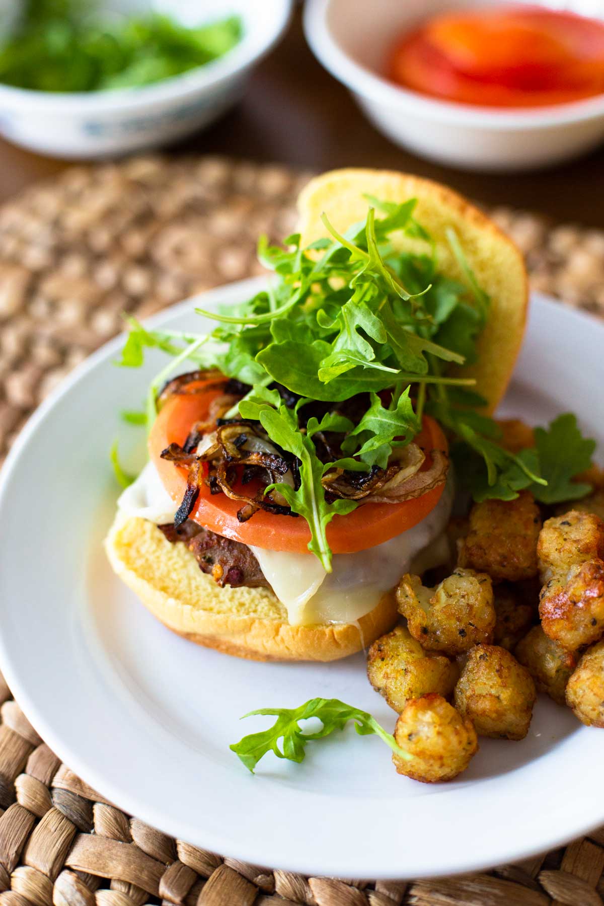 A turkey burger has cheese, tomato, and arugula piled up on top.