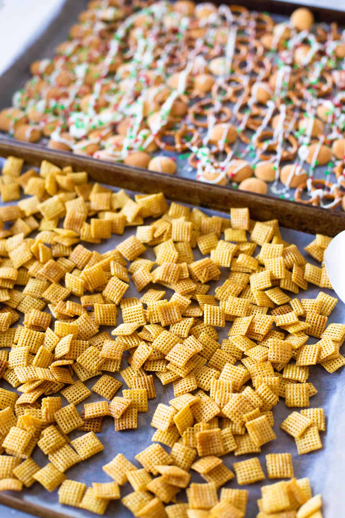 The Christmas chex mix is in the process of being prepped on two large baking sheets.