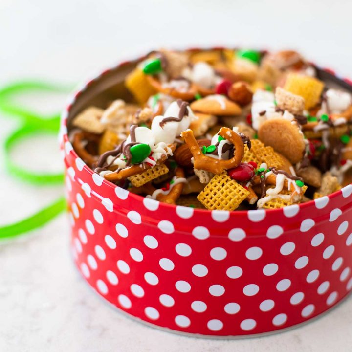 A red polka dot container has Christmas Chex Mix with red and green sprinkles over the top.
