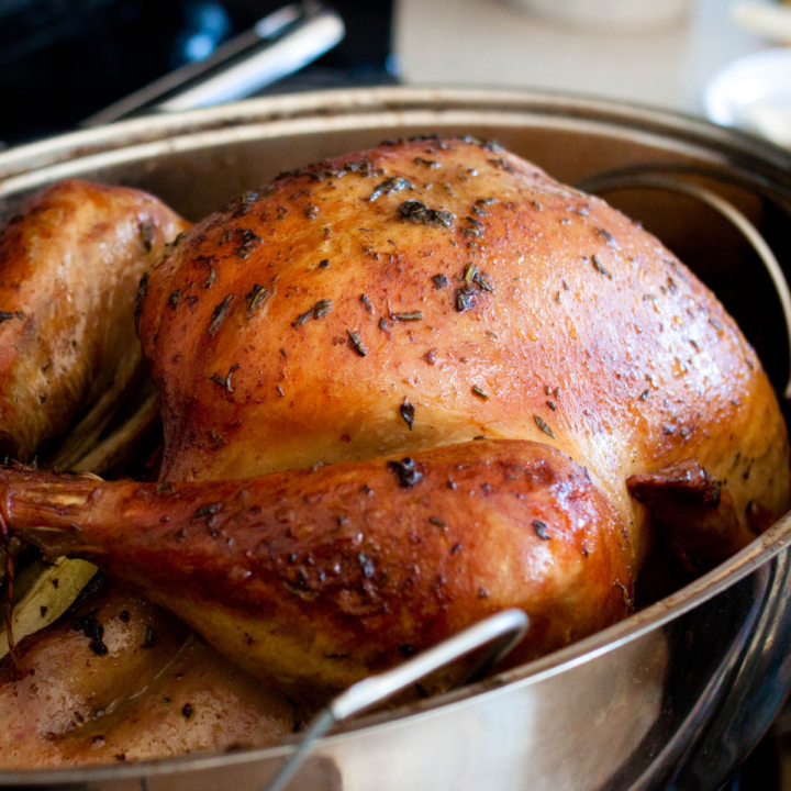 A roasted turkey sits in a metal roasting pan, golden brown all over.