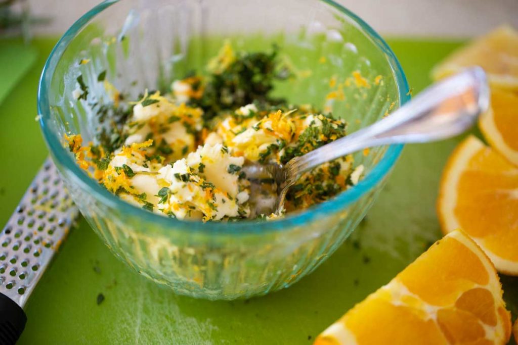 The herb butter for turkey has been mixed together in a small glass bowl. A grater and fresh oranges sit to the side.