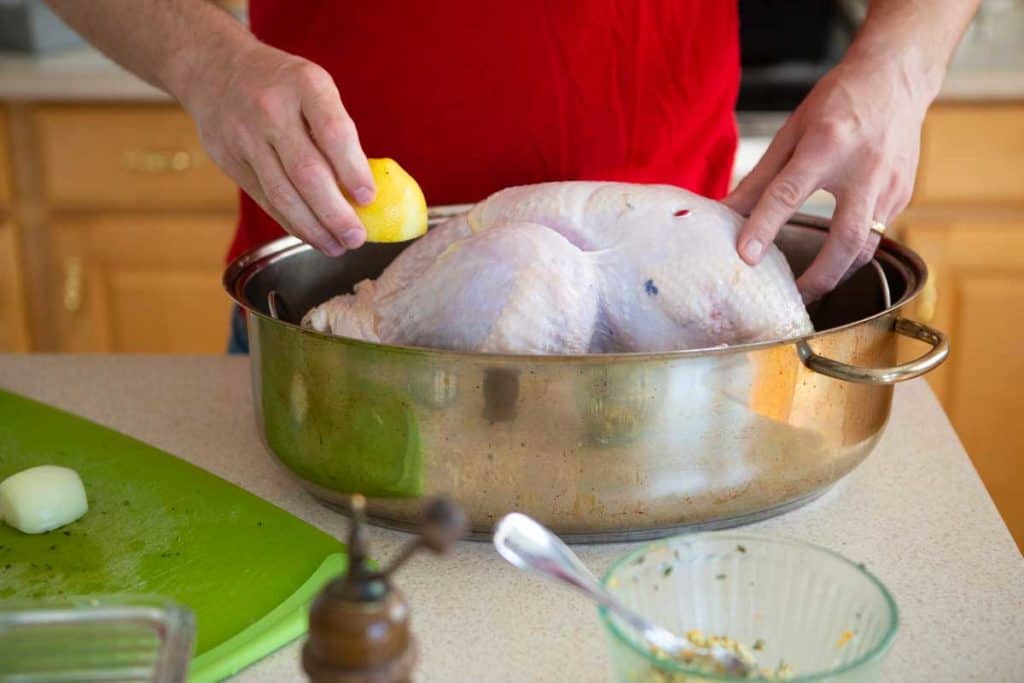 Hands are stuffing fresh lemon inside the turkey in a roasting pan.