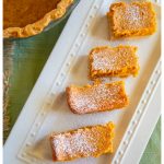 The pumpkin gooey butter cake bars are on a white platter with a pumpkin decoration.