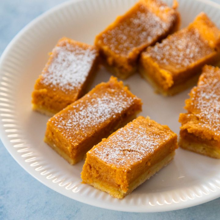The sliced pumpkin gooey butter cake bars are on a white plate. There's a dusting of powdered sugar over the top for garnish.