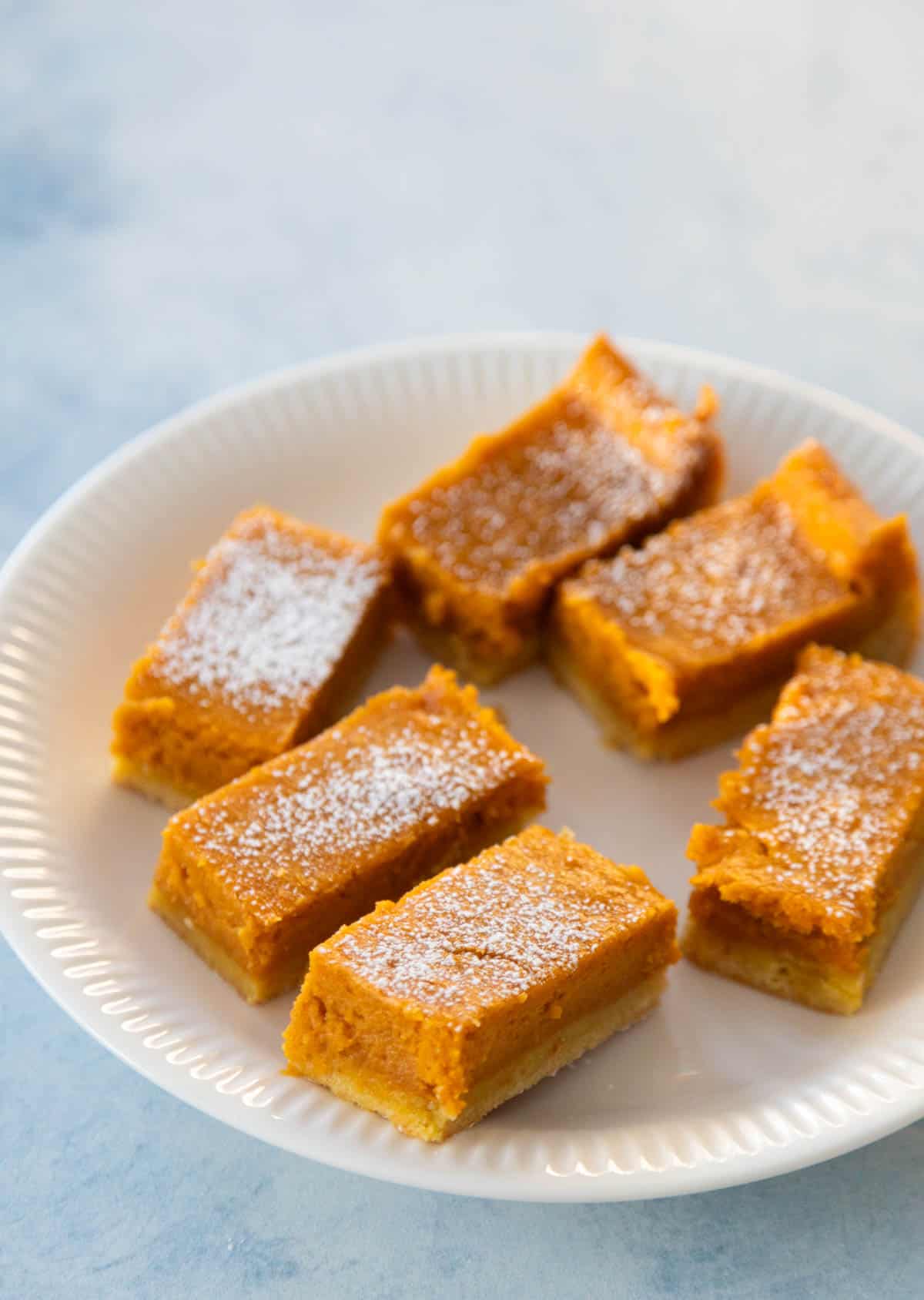 The finished pumpkin bars are on a white plate with powdered sugar on top.