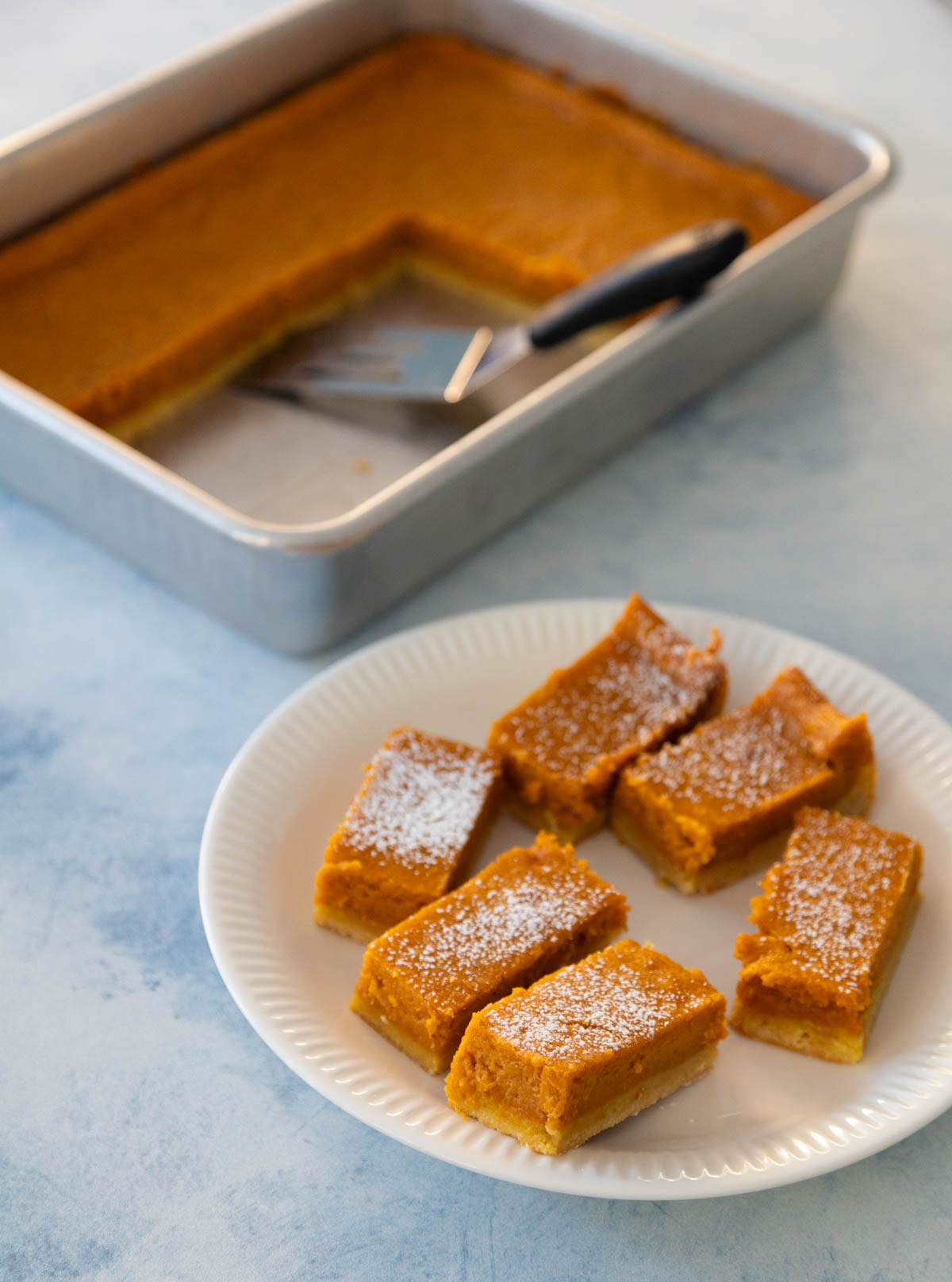 The plate of sliced pumpkin bars sits in front of the baking pan so you can see how neatly they slice.