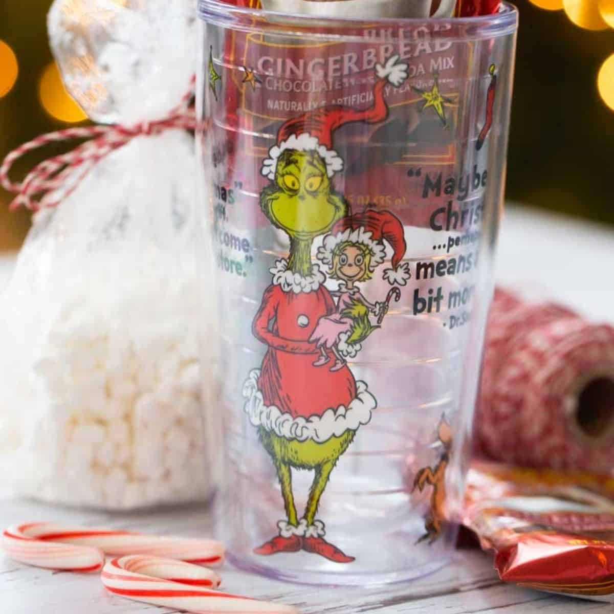 A Grinch tumbler with a bag of marshmallows and mini candy canes.