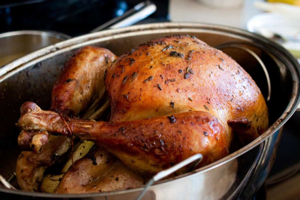 The finished roasted herb butter turkey rests in a roasting pan.