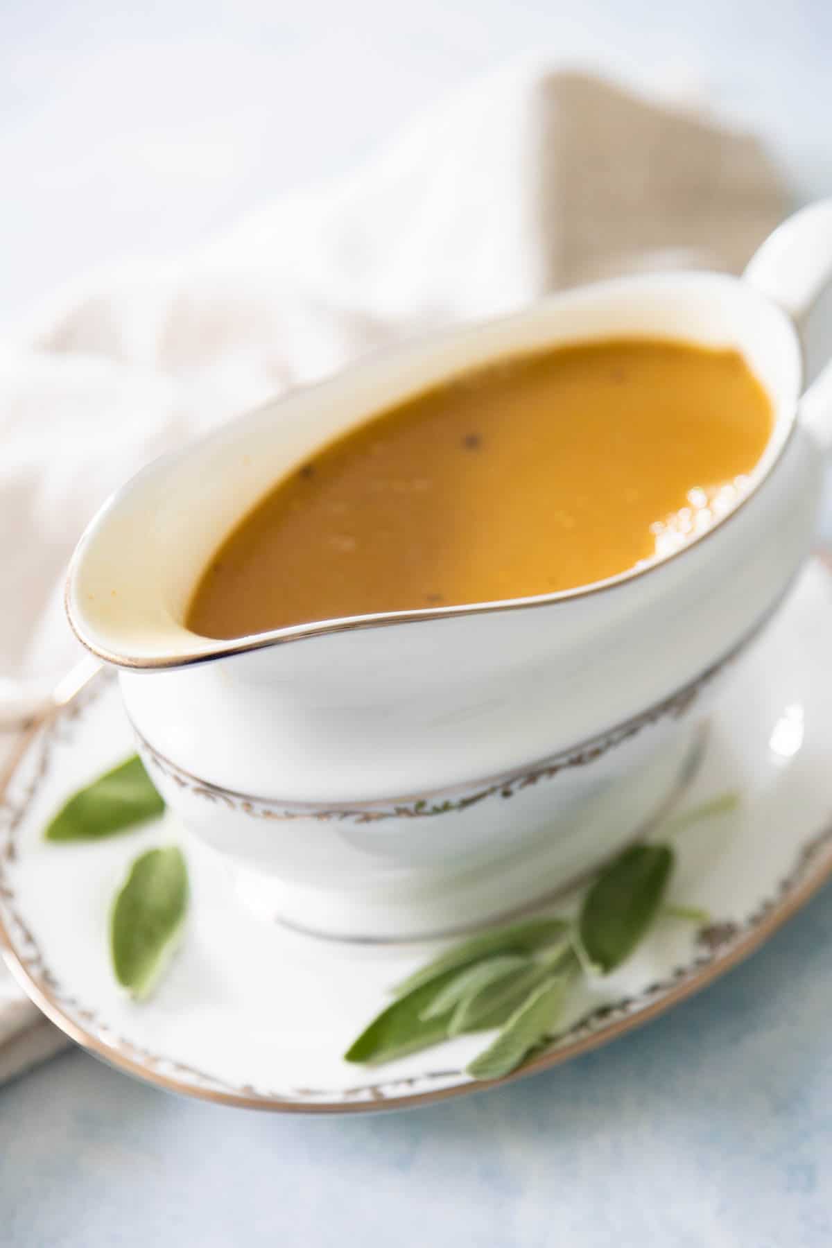 The turkey gravy is being served in a gravy boat with fresh sage on the side.