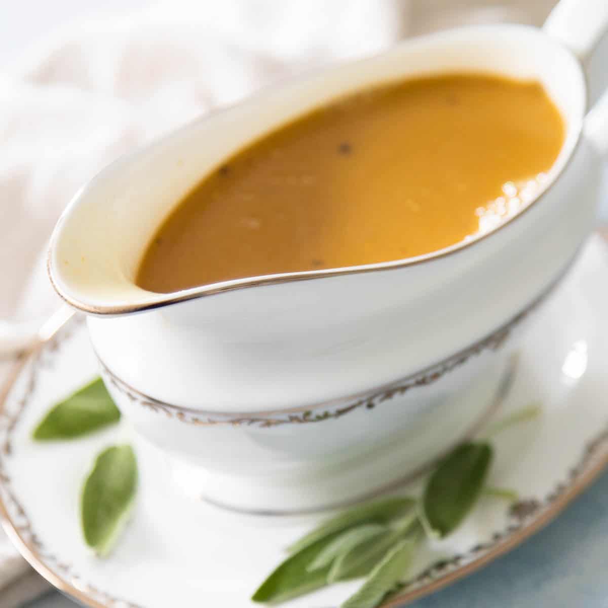 The turkey gravy is being served in a china gravy boat with fresh sage for garnish.