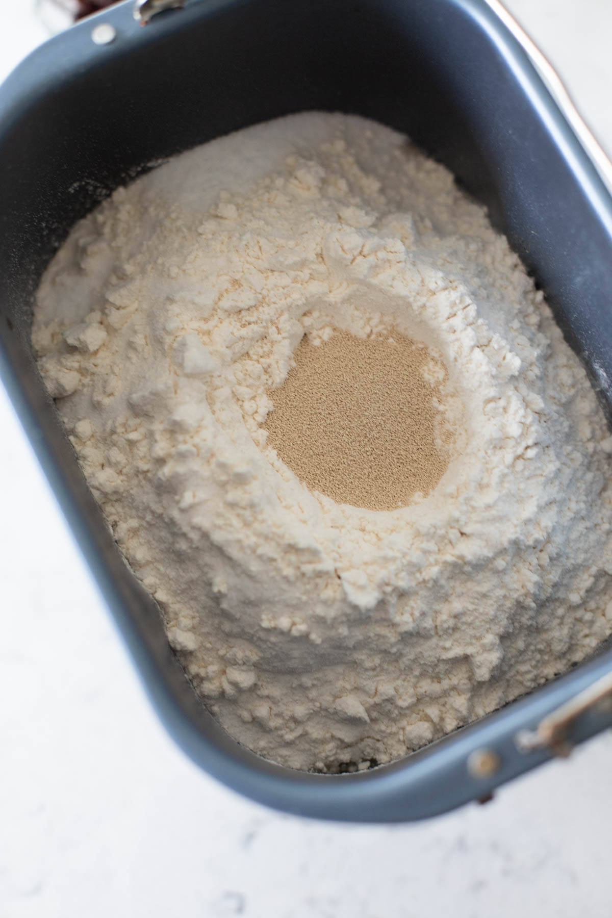 The bread pan is filled with flour and yeast.