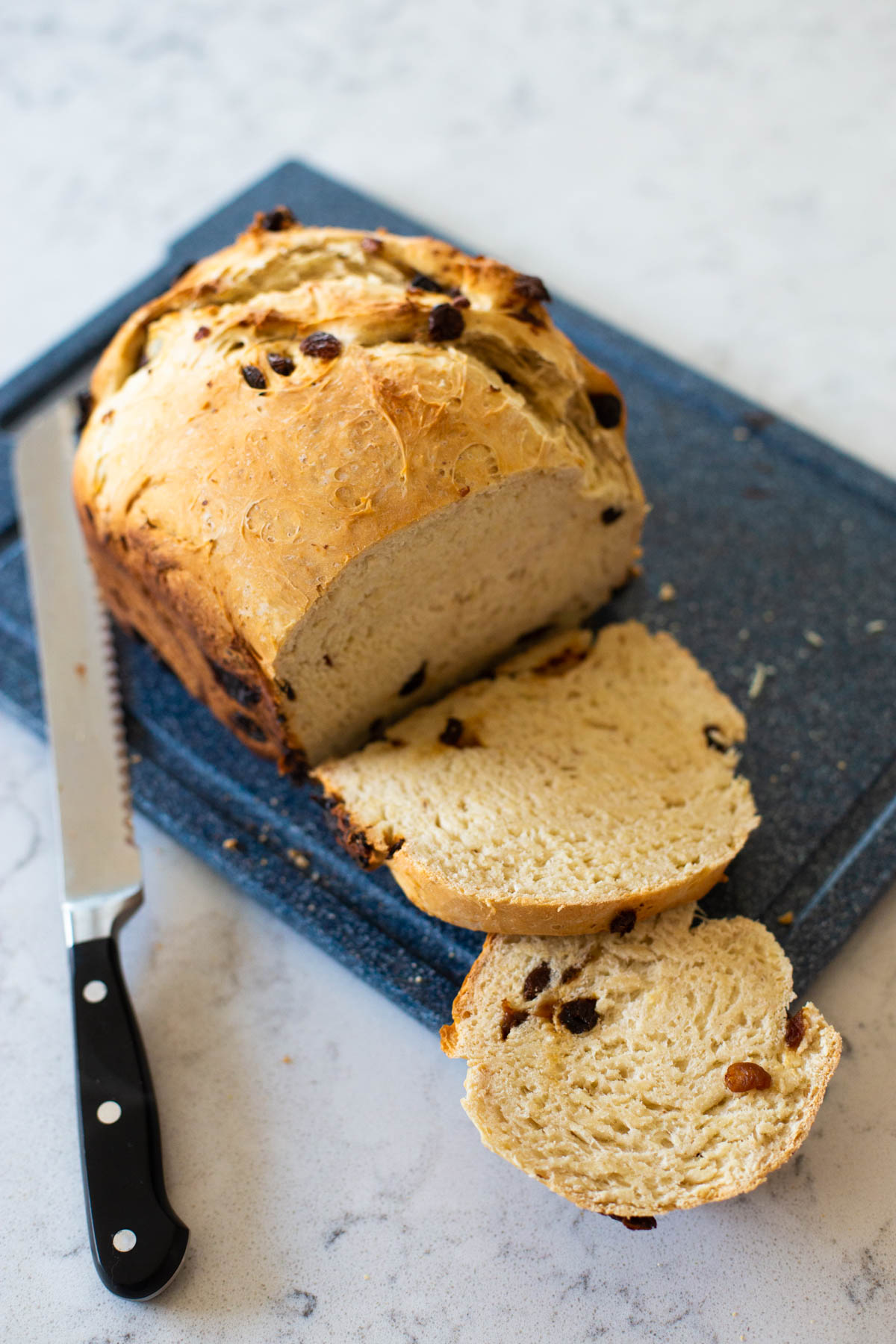 The raisin bread is on a cutting board and has been sliced with a long serrated bread knife.