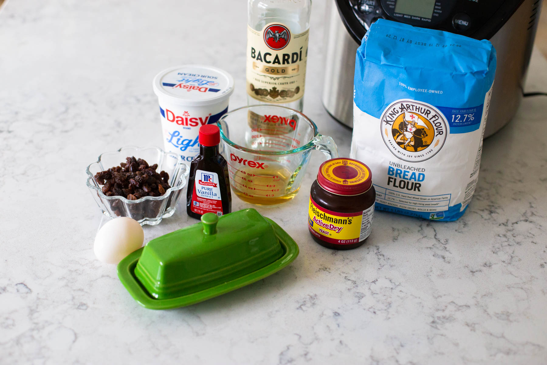 The ingredients to make the raisin bread in a bread maker are on the counter.
