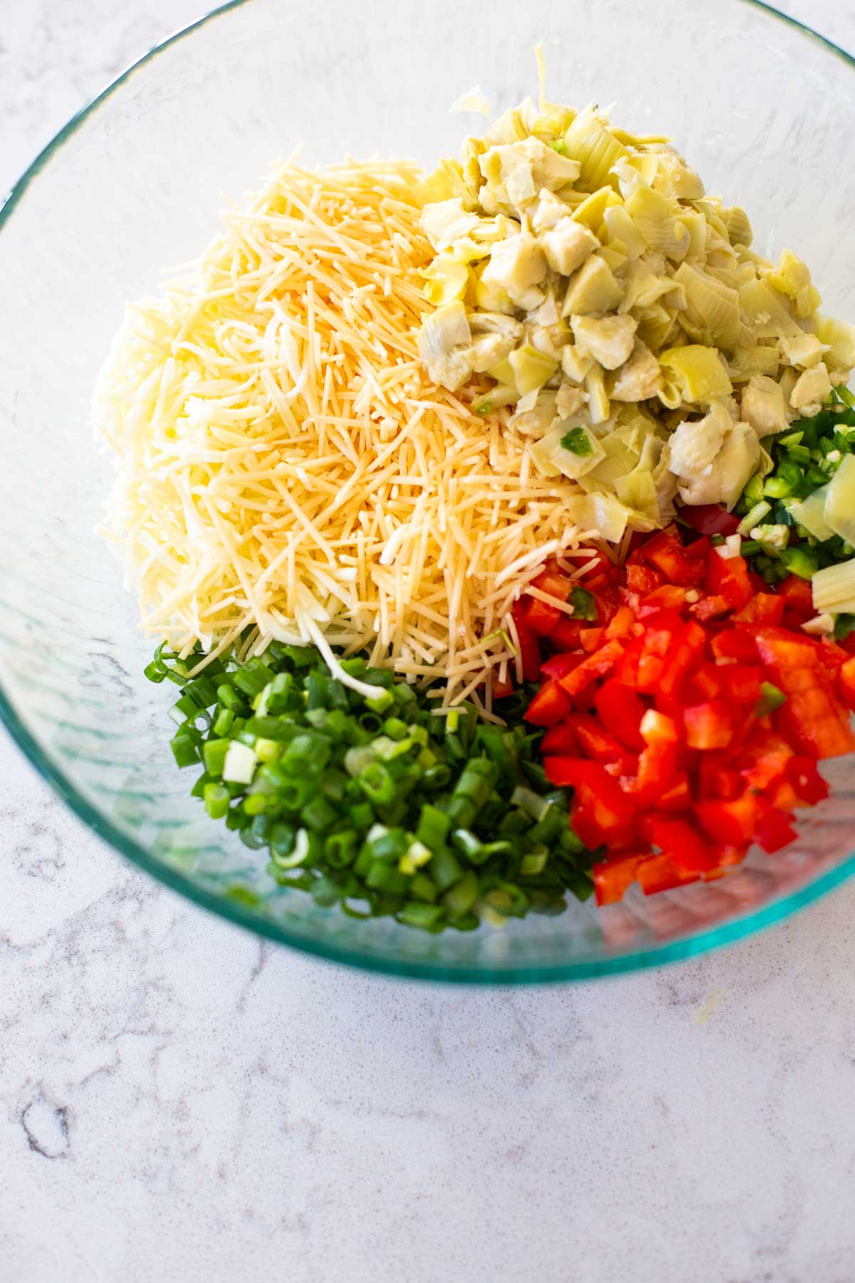 The minced jalapeño, artichoke hearts, and veggies are added to a bowl with shredded cheese.