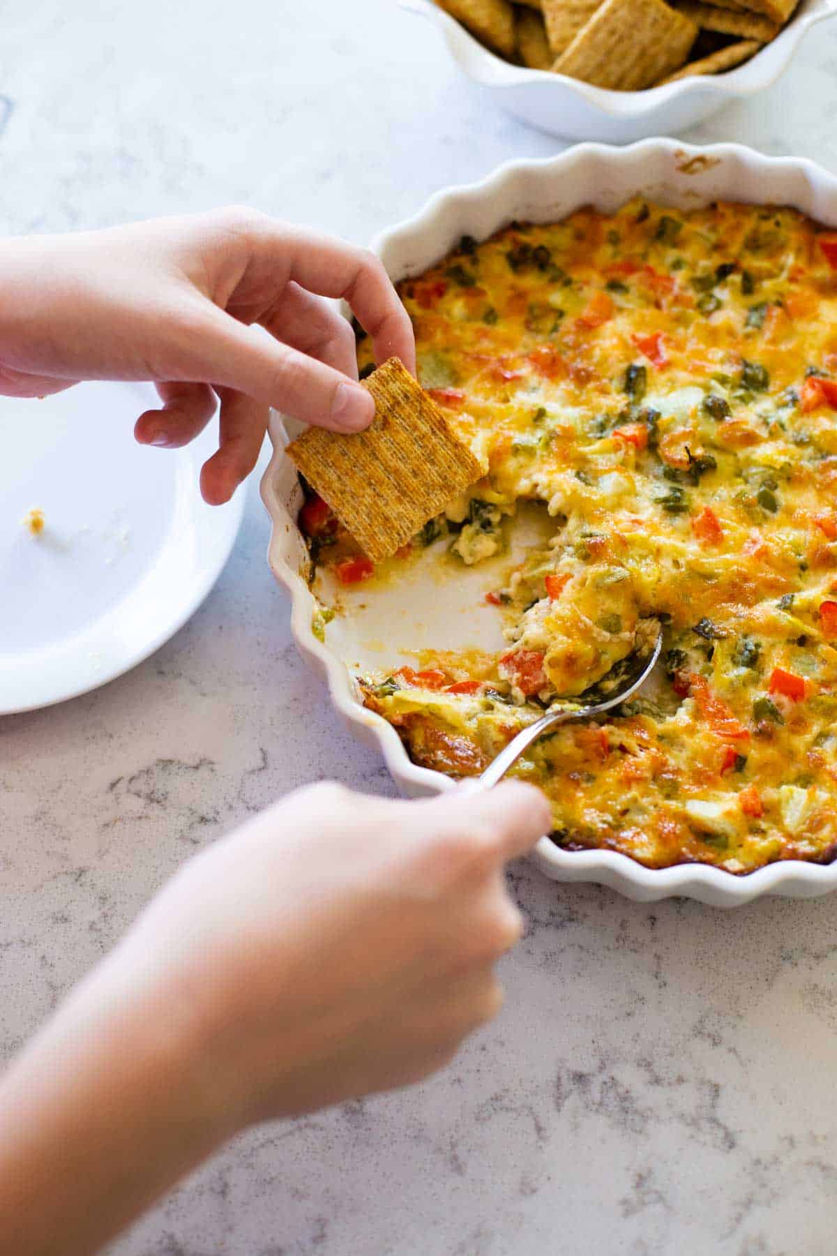 Two hands are scooping up the dip onto a cracker.