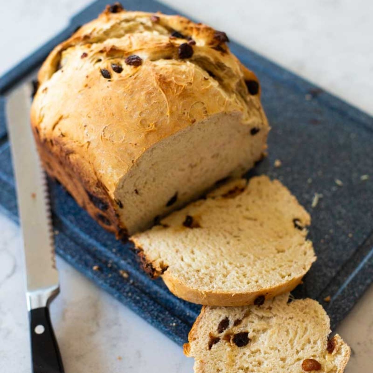 A warm loaf of rum raisin bread is sliced to serve.