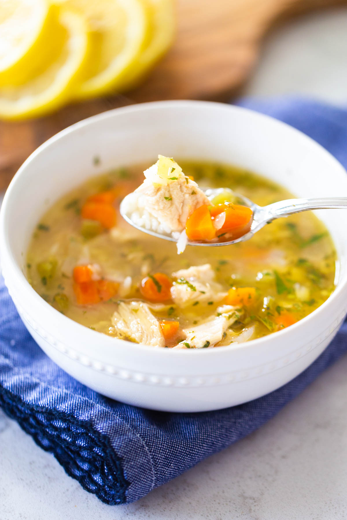 The white bowl is filled with classic chicken soup. A spoon is lifting up a bite with chicken on it.