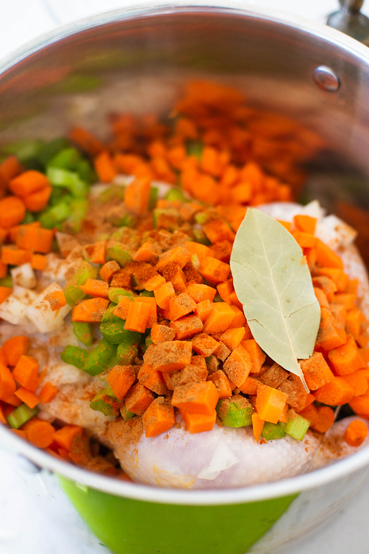 The chicken is in the pot with diced vegetables and bay leaves over the top.