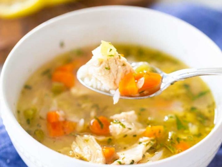 A bowl of homemade chicken soup with chicken and carrots has a spoon scooping up a bite.