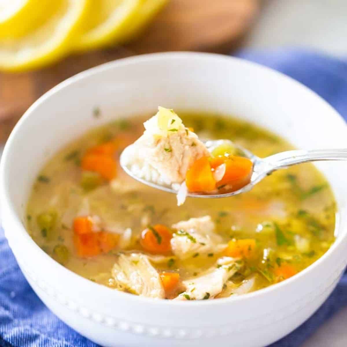 A bowl of homemade chicken soup with chicken and carrots has a spoon scooping up a bite.