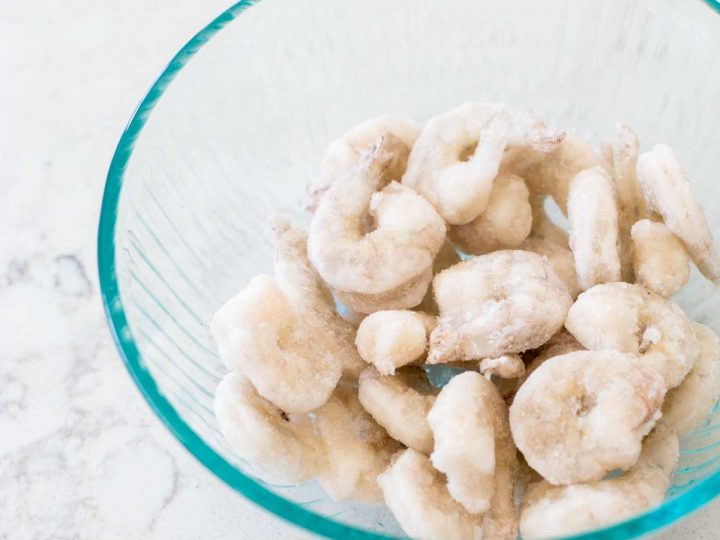 A clear mixing bowl is filled with frozen raw shrimp.