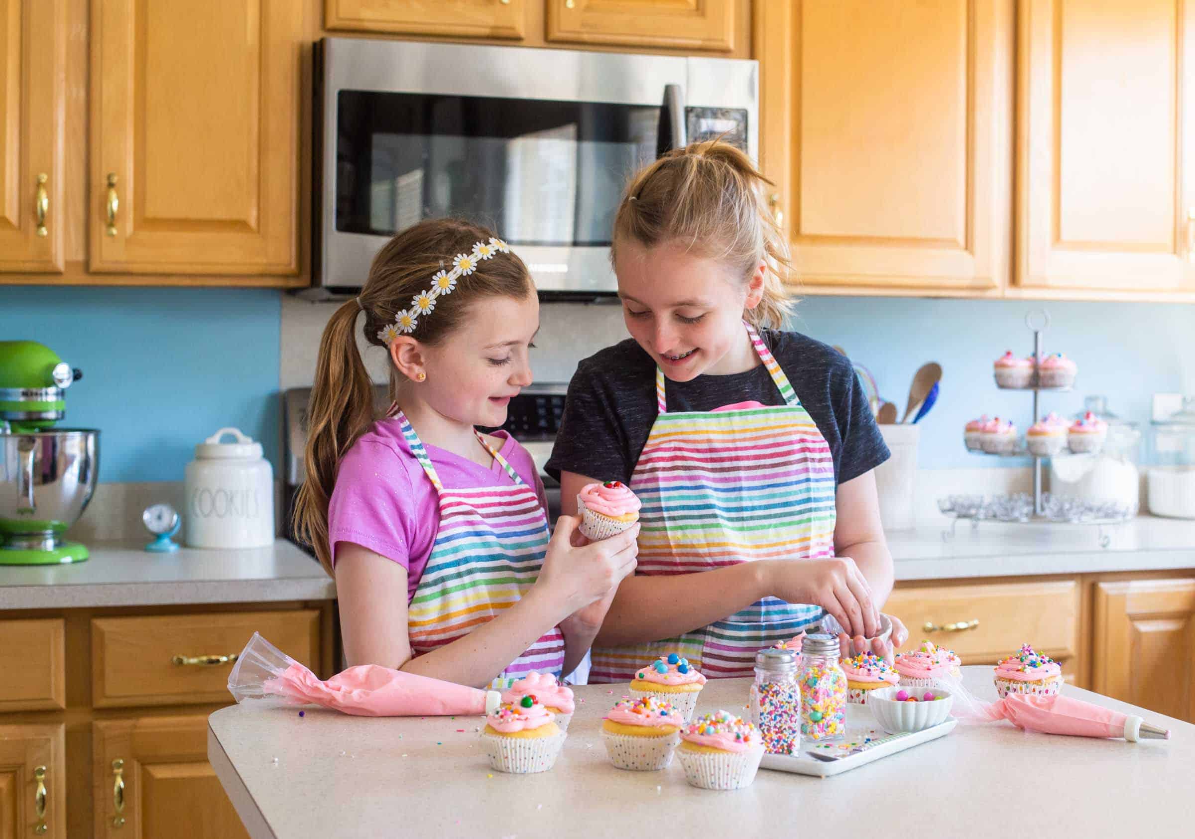 My two girls baking pink-frosted cupcakes in our kitchen as we test The Ultimate Kids' Baking Book recipes.