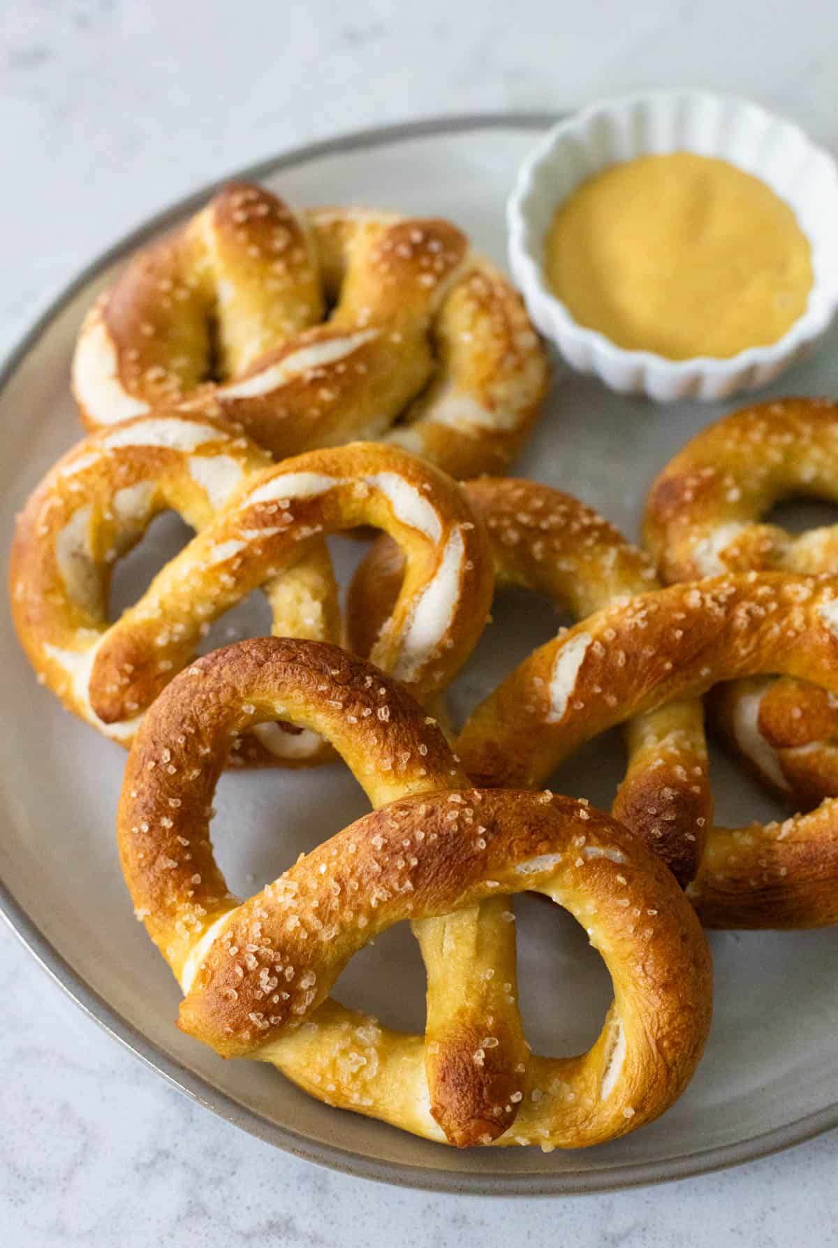 The plate of baked pretzels has a cup of honey mustard dipping sauce.